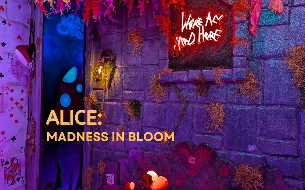 Alice: Madness in Bloom immersive escape room at Huddy’s Escape, featuring colorful playing cards, neon lighting, flowers, and a dark Wonderland-inspired setting.
