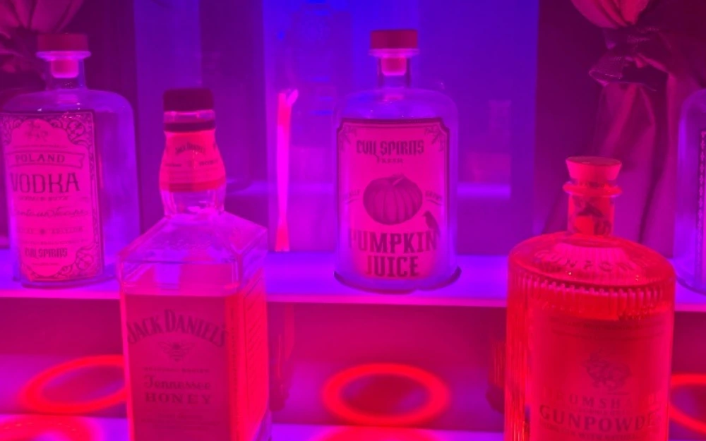 Assorted liquor and magic potion bottles bathed in pink neon light inside the Chronowhiskey escape room at Huddy's Escape in Gainesville, Florida.