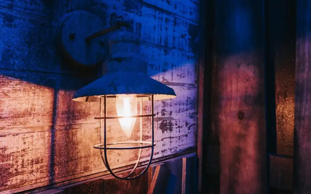 Vintage industrial cage wall lantern glowing over rustic wooden paneling in the Nineteen70 escape room game at Huddy's Escape in Ocala, Florida.