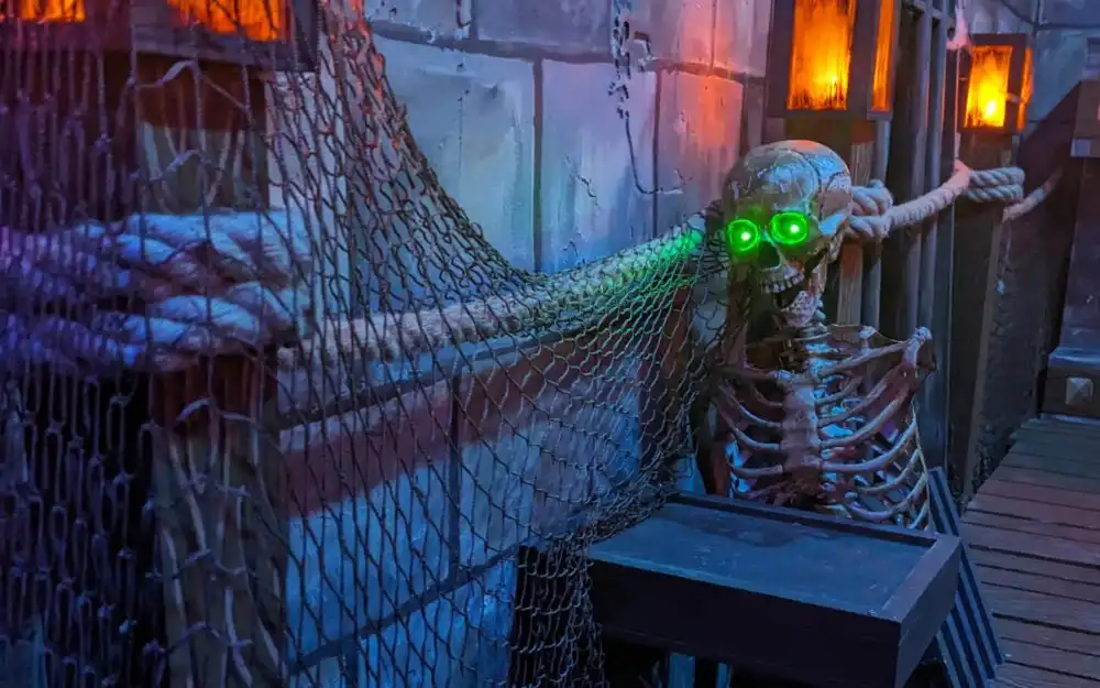Glowing green-eyed skeleton prop tangled in nautical netting inside the Tomb of Tales escape room at Huddy's Escape in Ocala, Florida.